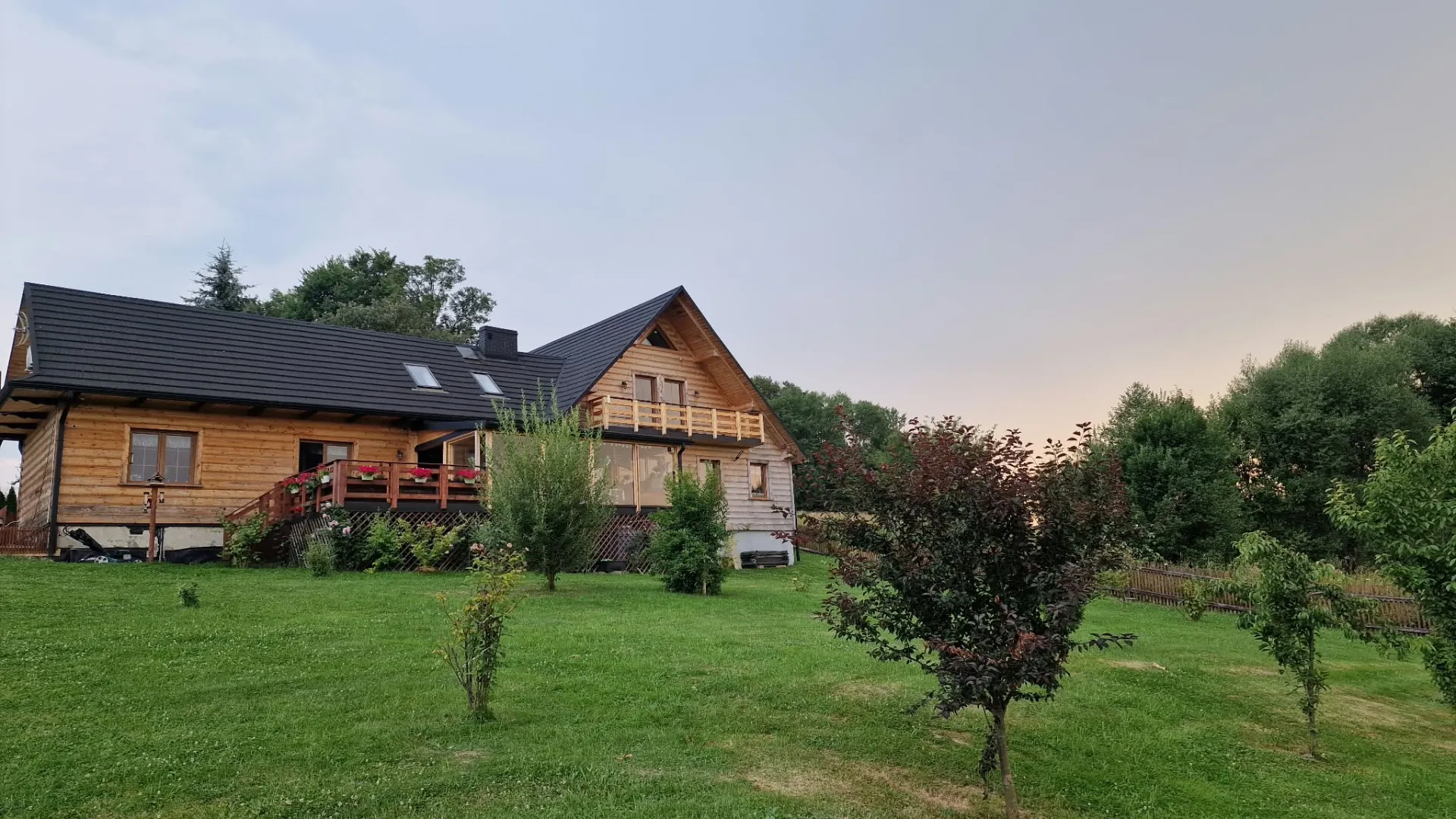 Drewniany dom Kluskówka od strony ogrodu, widok z tarasem i zielonym trawnikiem