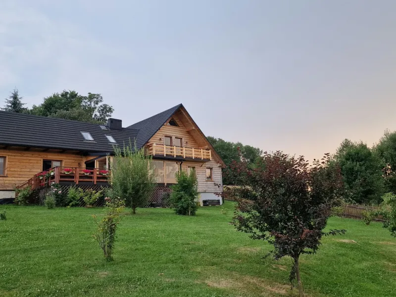 Drewniany dom Kluskówka od strony ogrodu, widok z tarasem i zielonym trawnikiem