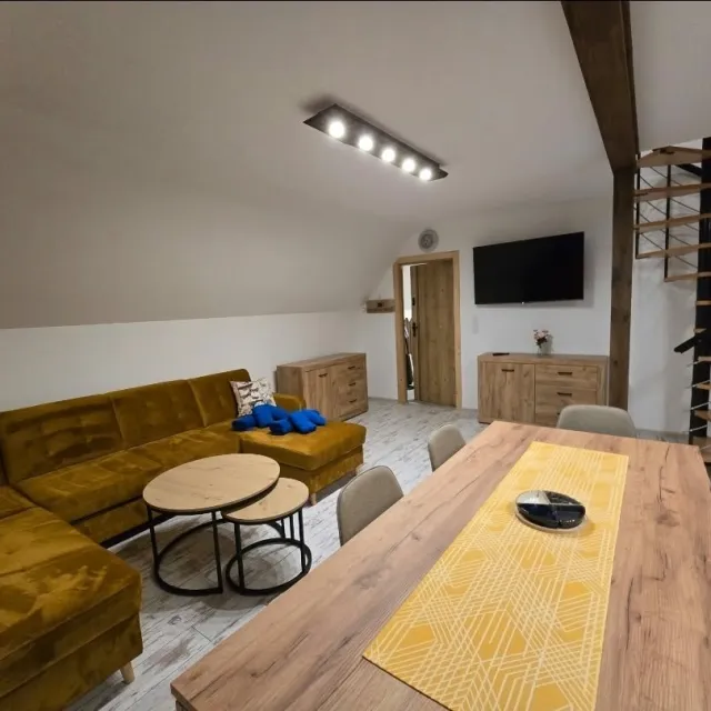 Salon z dużym stołem na 6 osób, narożnikiem i schodami na poddasze w apartamencie Niebieskim
