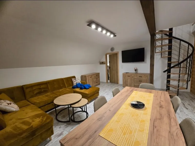 Salon z dużym stołem na 6 osób, narożnikiem i schodami na poddasze w apartamencie Niebieskim