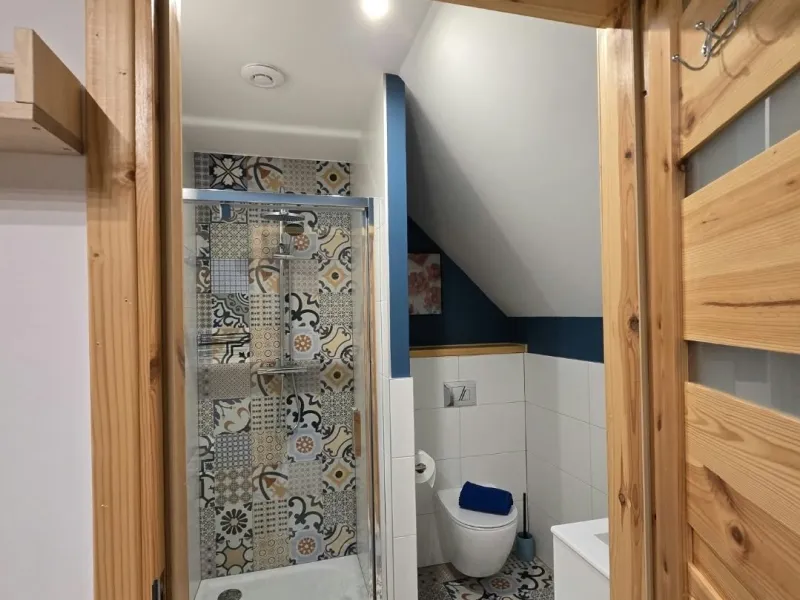 Łazienka z prysznicem widoczna przez drewniane drzwi w apartamencie Niebieskim