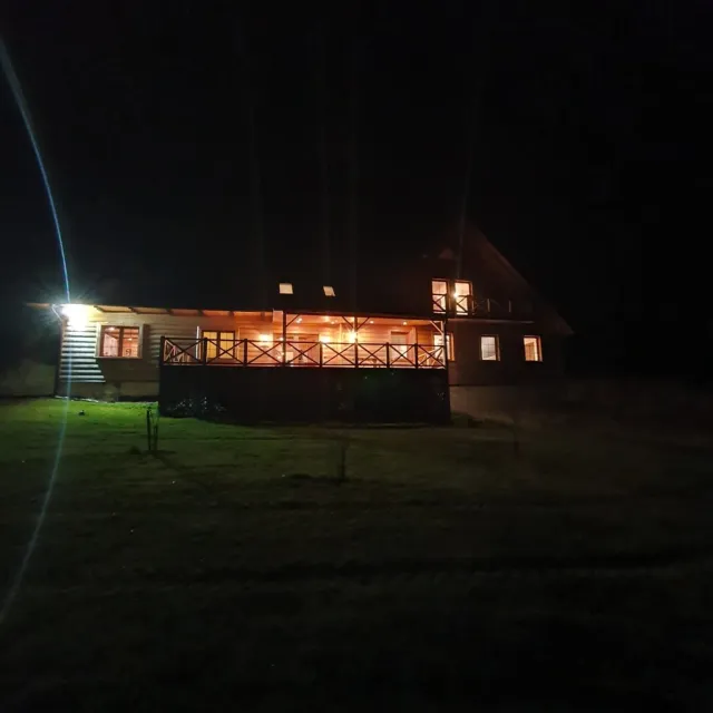 Drewniany dom Kluskówka nocą, rozświetlony, widziany z ogrodu