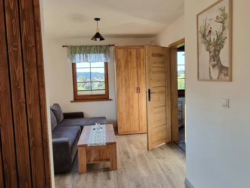 Salon w apartamencie Szarym z rozkładaną kanapą, drewnianymi drzwiami i obrazem jelenia na ścianie